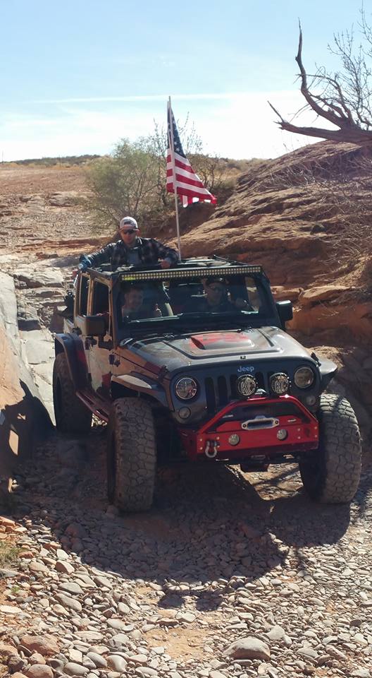Black Jeep Wrangler off-roading with an American flag on the roof rack.