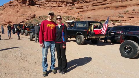 1979 Ford Bronco - A man and a woman stand in front of a black 1979 Ford Bronco with an American flag attached to the tailgate. Several other off-road vehicle…