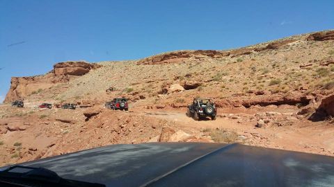 1979 Ford Bronco - A convoy of off-road vehicles, including Jeeps, navigates a rocky, desert trail under a clear blue sky. The foreground shows the hood and w…