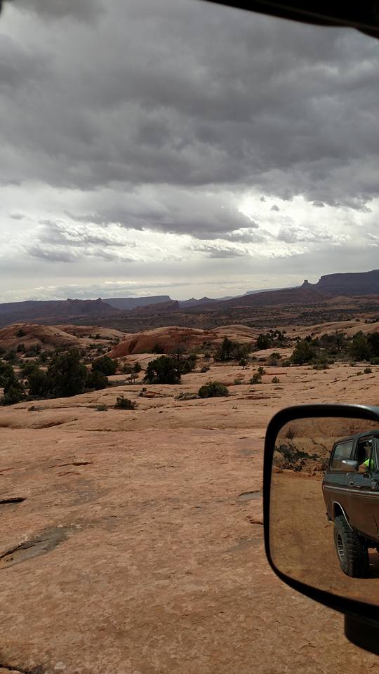 Side mirror reflection of a dark SUV on a rocky desert landscape.