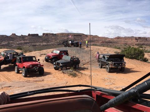 1979 Ford Bronco - A group of Jeeps and a Ford Bronco are parked on a dusty, rocky trail with red rock formations in the background. The Bronco has its hood o…