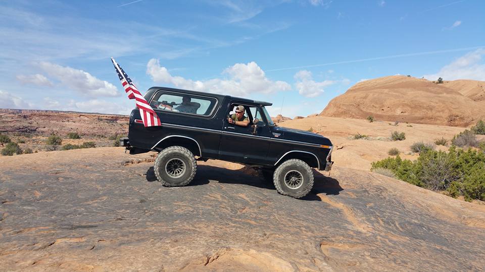 Black Ford Bronco driving on a rocky desert terrain with an American flag.