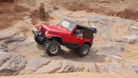 1979 Ford Bronco - A red Jeep Wrangler is navigating a rocky, off-road trail in a desert landscape. The driver is visible behind the wheel, and the vehicle is…