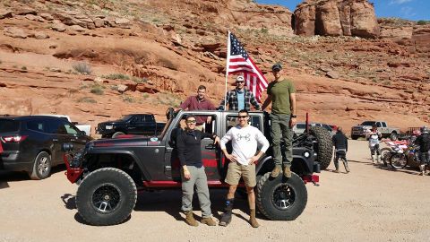 1979 Ford Bronco - A group of people pose with an American flag in front of a modified Jeep Wrangler in a desert landscape with rocky cliffs in the background…