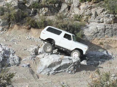 1979 Ford Bronco - A white Ford Bronco is navigating a rocky, off-road trail with steep inclines and large boulders. The vehicle is angled on the terrain, wit…