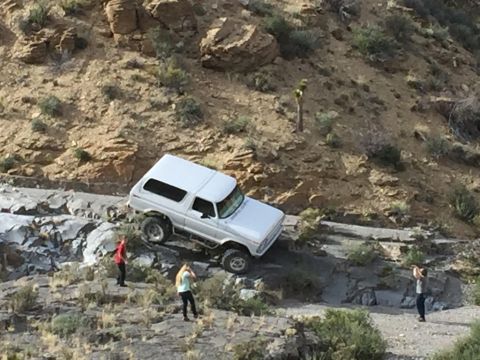 1979 Ford Bronco - A white Ford Bronco is parked on a rocky, off-road trail with three people standing nearby. The vehicle is angled on the uneven terrain, wi…