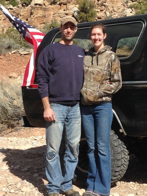 1979 Ford Bronco - A couple stands in front of a black 1979 Ford Bronco with an American flag attached to the rear. The vehicle is parked on a rocky, outdoor…