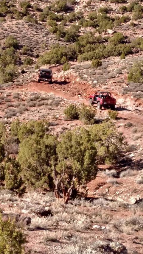 1979 Ford Bronco - Two off-road vehicles navigate a dusty, arid trail. A black SUV is in the foreground, followed by a red off-road vehicle further up the pat…
