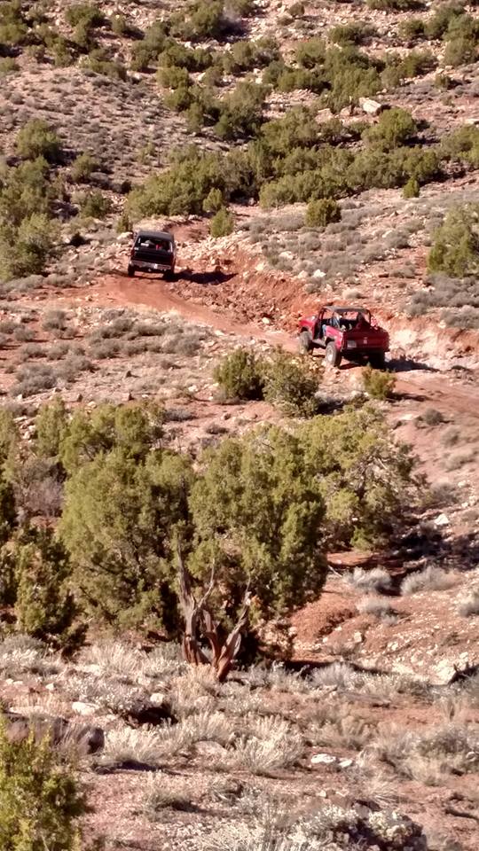 Two off-road vehicles on a dusty trail in a desert landscape.