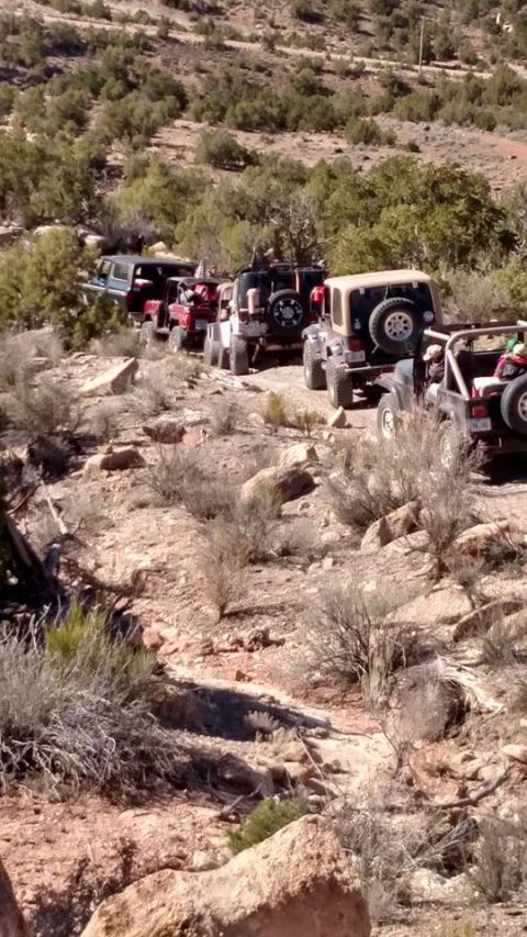 1979 Ford Bronco - A line of off-road vehicles, primarily Jeeps, navigates a rocky, arid trail on a sunny day. The vehicles are positioned at various angles o…