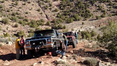 1979 Ford Bronco - A group of people are gathered around a black 1979 Ford Bronco and a red off-road vehicle on a dirt trail in a rocky, arid landscape. The B…