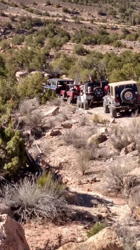 1979 Ford Bronco - A line of off-road vehicles, including a dark blue SUV and several Jeeps, navigate a rocky, arid trail. The vehicles are positioned on a di…