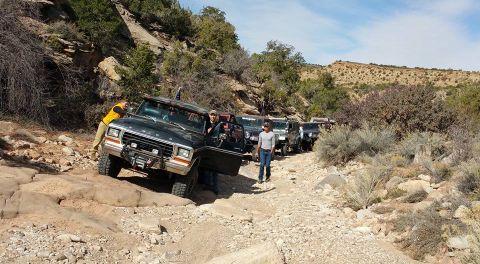 1979 Ford Bronco - A group of off-road vehicles, including a black Ford Bronco, navigate a rocky, desert trail under a bright blue sky.