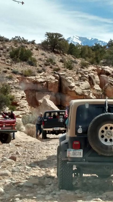 1979 Ford Bronco - A group of off-road vehicles, including a black Ford Bronco and a tan Jeep, are parked on a rocky, desert trail with a snow-capped mountain…