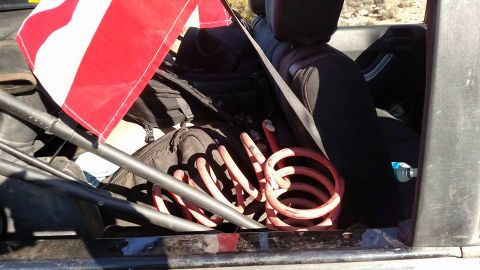 1979 Ford Bronco - The interior of a vehicle, likely a Jeep Wrangler, is filled with gear including backpacks and a red coil spring. An American flag is attac…