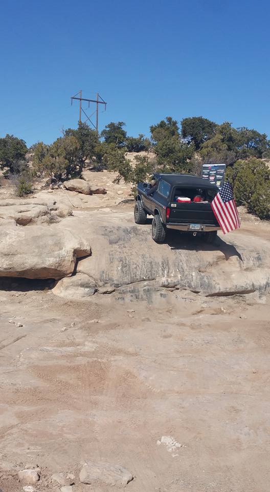 Black Ford Bronco parked on rocks with an American flag.