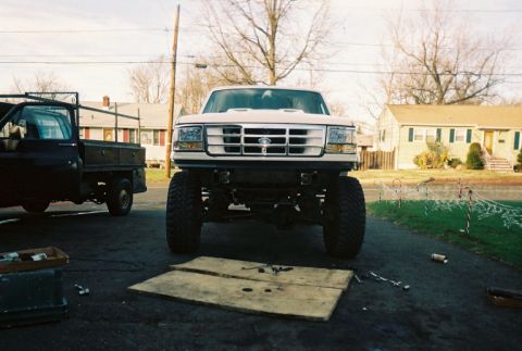 1996 Ford C-250 (Centurion Conversions) - A lifted white Ford F-250 is parked in front of houses, with another truck to its left.
