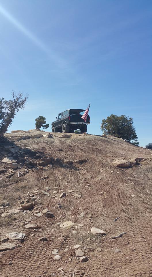 Black SUV with American flag on a dirt hill.