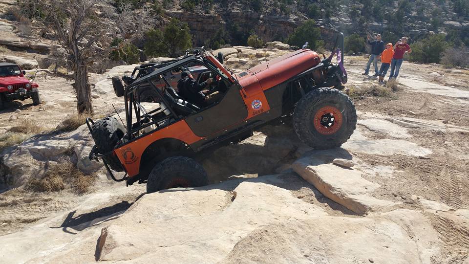 Orange Jeep Wrangler climbing a rocky off-road trail.