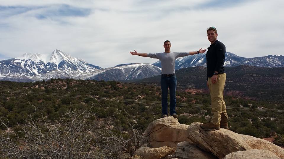 Two men standing on rocks with mountains in the background.
