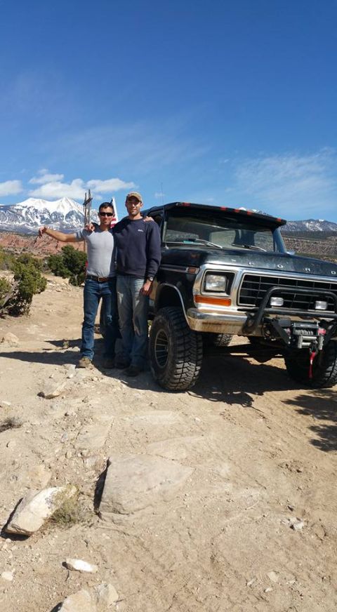 1979 Ford Bronco - Two men pose with a black 1979 Ford Bronco with large off-road tires and a winch mounted on the front bumper. The vehicle is parked on a di…