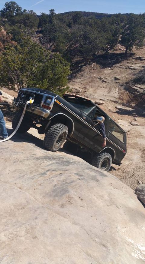 1979 Ford Bronco - A black 1979 Ford Bronco is angled on a rocky incline, with a winch line attached to the front bumper and a person visible in the driver's…