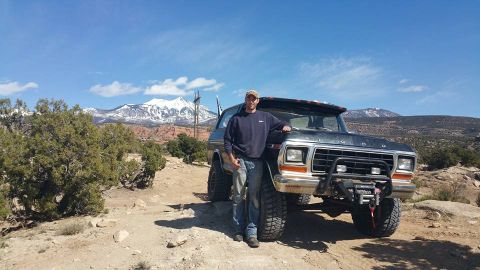 1979 Ford Bronco - A man stands next to a dark colored Ford Bronco with large off-road tires and a winch mounted on the front bumper. The vehicle is parked on…