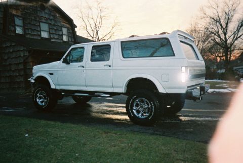 1996 Ford C-250 (Centurion Conversions) - This lifted SUV, possibly a 1996 Ford C-250 Centurion Conversions, is shown with a camper shell and custom wheels.
