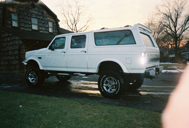 Lifted white four-door Ford Centurion conversion SUV on chrome wheels, rear three-quarter view at dusk