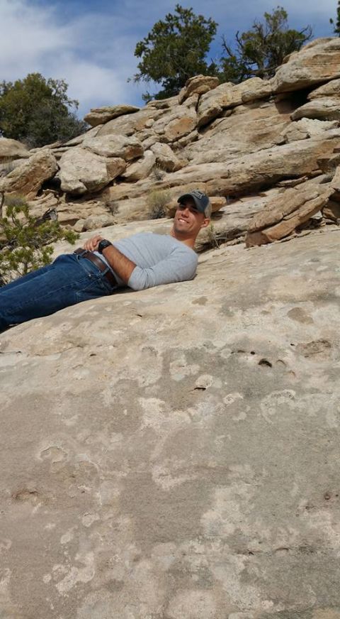1979 Ford Bronco - A man in a grey long-sleeved shirt and blue jeans is lying on a large rock formation, looking up and smiling. The background shows more roc…