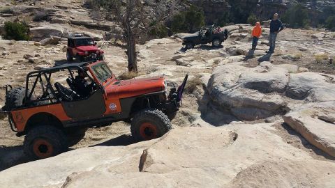 1979 Ford Bronco - An orange Jeep Wrangler with a roll cage is navigating a rocky off-road trail. A red Jeep Wrangler is visible in the background, also on th…