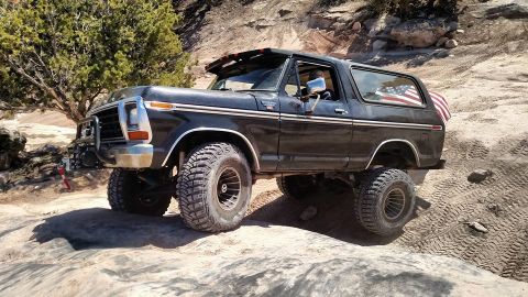 1979 Ford Bronco - A black, lifted 1979 Ford Bronco is navigating a rocky, off-road trail with an American flag displayed in the rear window.