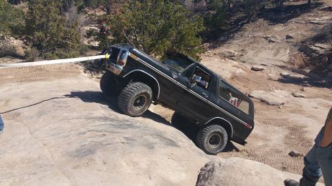 1979 Ford Bronco - A black 1979 Ford Bronco is navigating a rocky, off-road trail. The vehicle is angled steeply, with its tires gripping the uneven terrain.