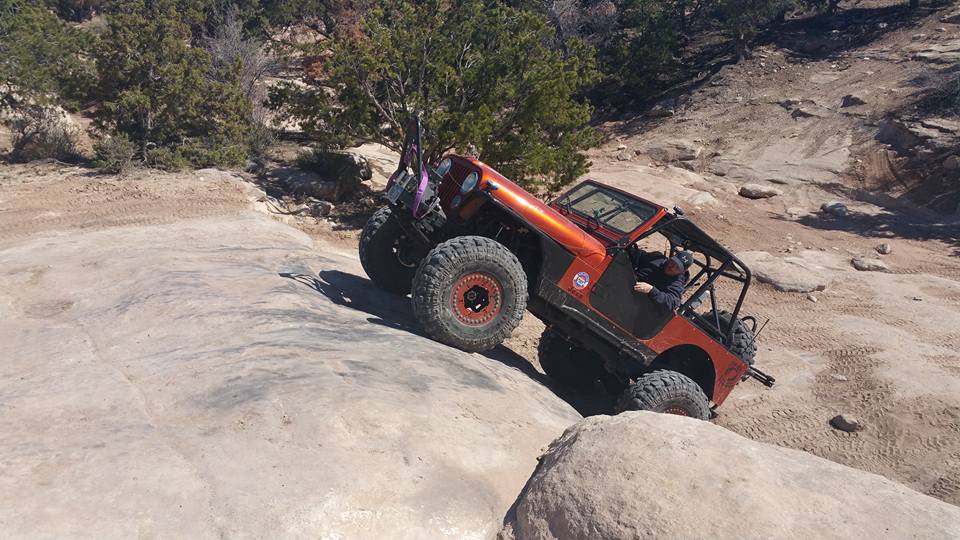 Orange Jeep Wrangler climbing a rocky off-road trail.
