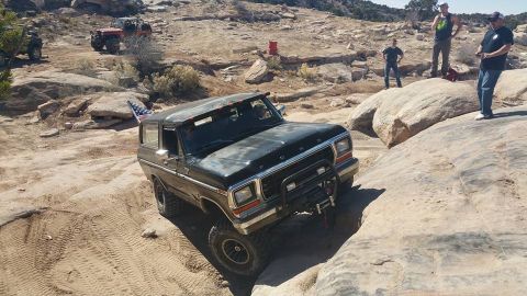 1979 Ford Bronco - A dark-colored, two-door Ford Bronco is navigating a rocky, off-road trail. The vehicle has a winch mounted on the front bumper and an Amer…