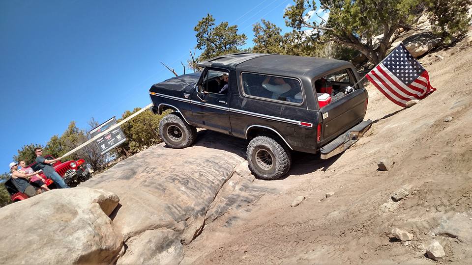 Black 1979 Ford Bronco climbing a rocky trail with an American flag.