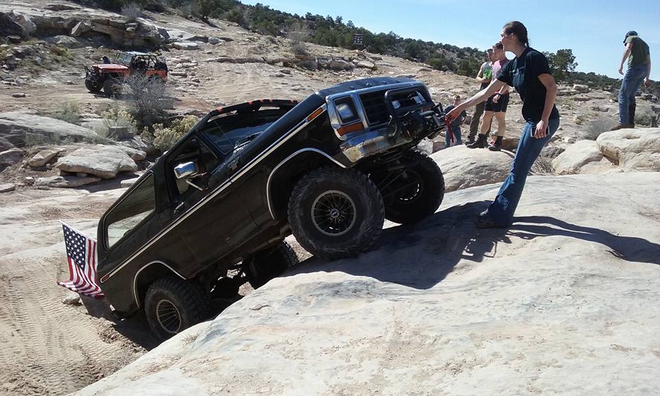 Black 1979 Ford Bronco climbing a rocky hill with people watching.
