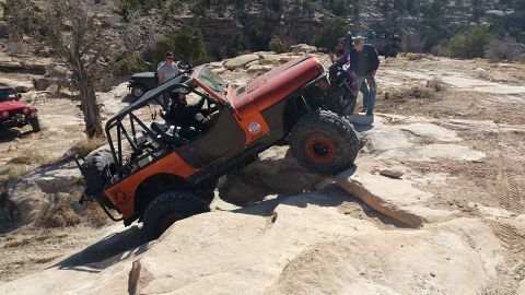 1979 Ford Bronco - An orange Jeep Wrangler with a roll cage is navigating a rocky obstacle course. Another red Jeep is visible in the background.