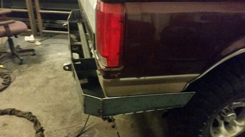 Custom metal bumper being installed on the rear corner of a dark red Ford Bronco.