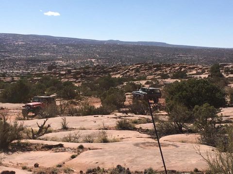 1979 Ford Bronco - Two off-road vehicles are parked on a rocky, desert landscape under a clear blue sky. A red Jeep Wrangler is visible on the left, and a dar…