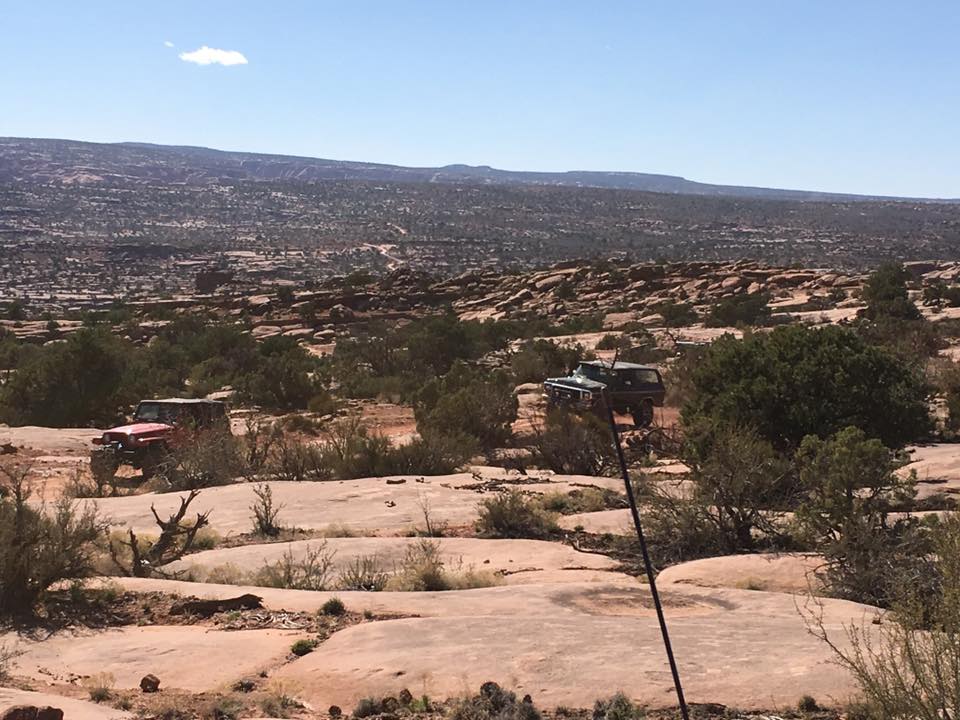 Red Jeep Wrangler and dark green Ford Bronco in a rocky desert landscape.