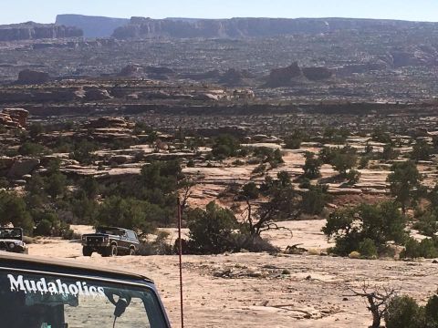 1979 Ford Bronco - A dark colored 1979 Ford Bronco is parked in a desert landscape with rocky terrain and sparse vegetation. The front of another vehicle with…