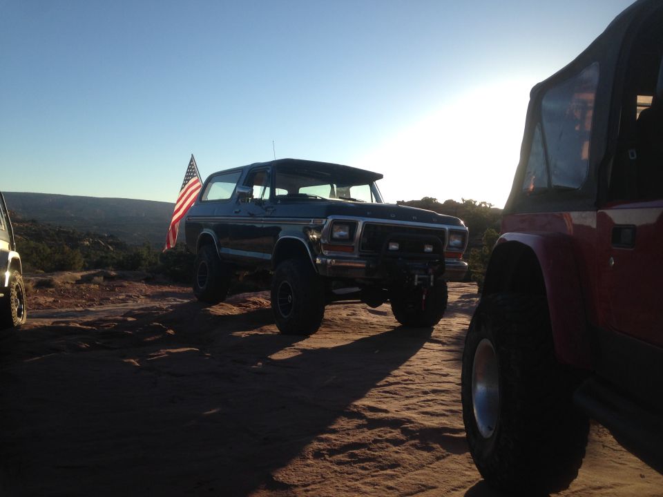 1979 Ford Bronco with American flag parked on desert landscape.