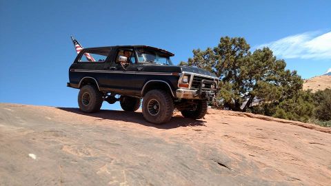 1979 Ford Bronco - A black 1979 Ford Bronco is parked on a rocky, desert landscape under a clear blue sky. An American flag is visible in the rear window.