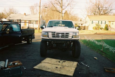 1996 Ford C-250 (Centurion Conversions) - Front view of a lifted white Ford F-Series truck with a flatbed truck beside it.