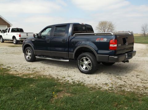 2005 Ford F-150 - A dark blue Ford F-150 pickup truck is parked on a gravel driveway next to a grassy area. A white Ford F-150 pickup truck is parked behind…