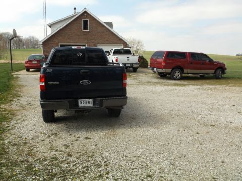 2005 Ford F-150 - Multiple vehicles including a 2005 Ford F-150 are parked in a gravel driveway outside a brick house.