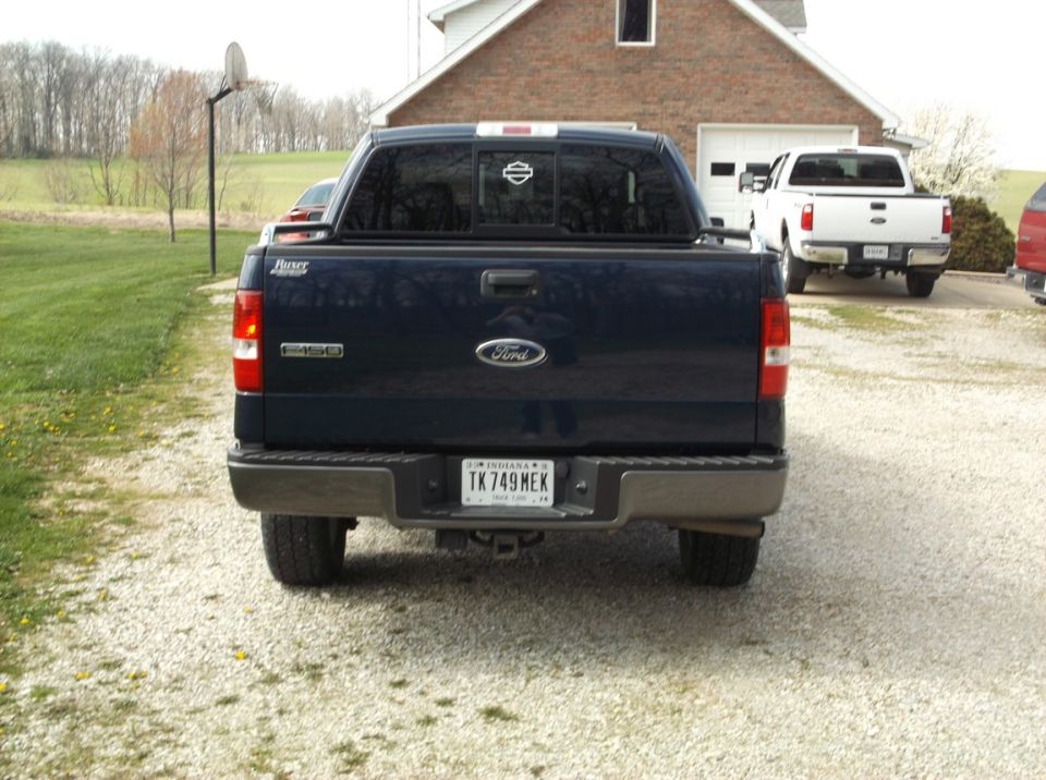 Rear view of a dark blue Ford F-150 pickup truck. Another white truck is parked behind it