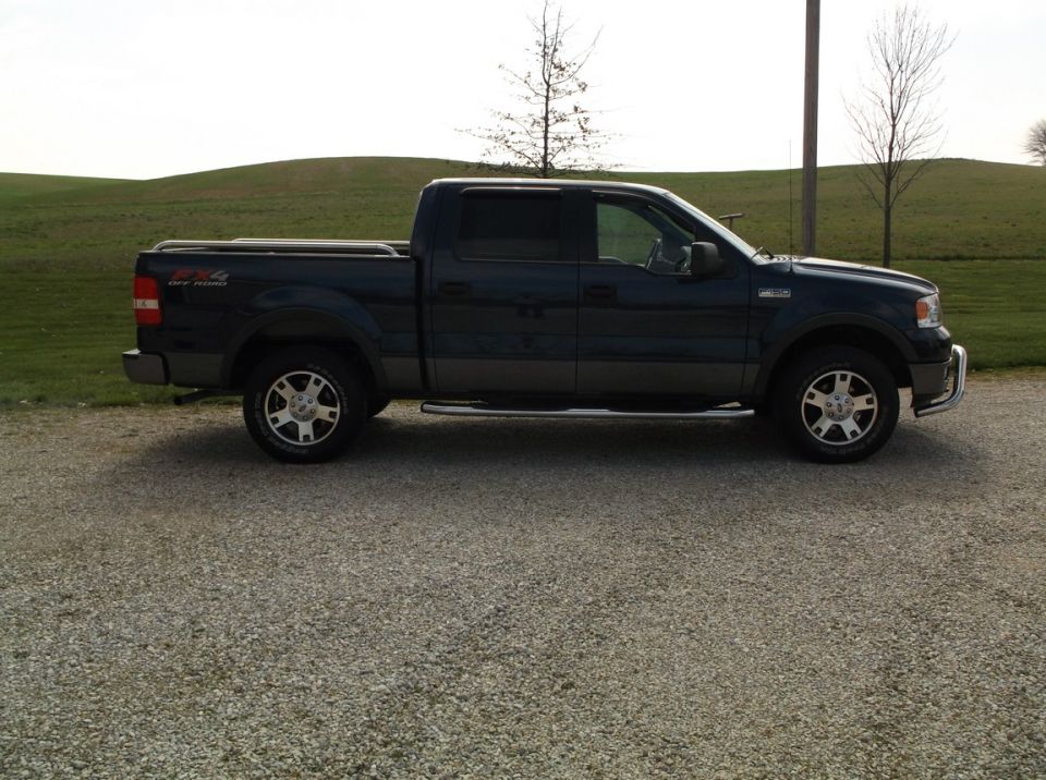 Dark blue pickup truck parked on gravel, side view. Has a chrome bumper and running boards