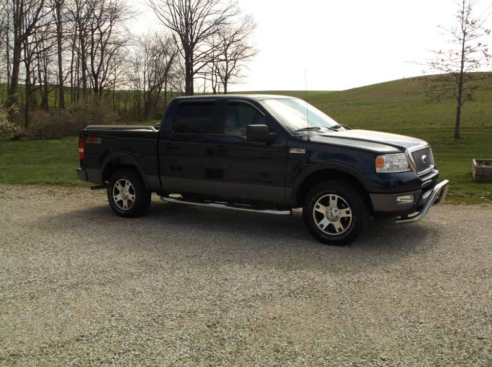 Dark blue Ford F-150 pickup truck, front quarter view, parked on gravel. Chrome bull bar on front bumper